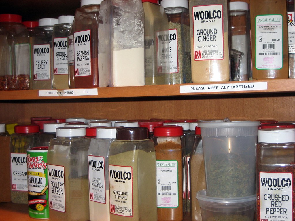 Large labeled spice containers arranged on wooden kitchen shelves
