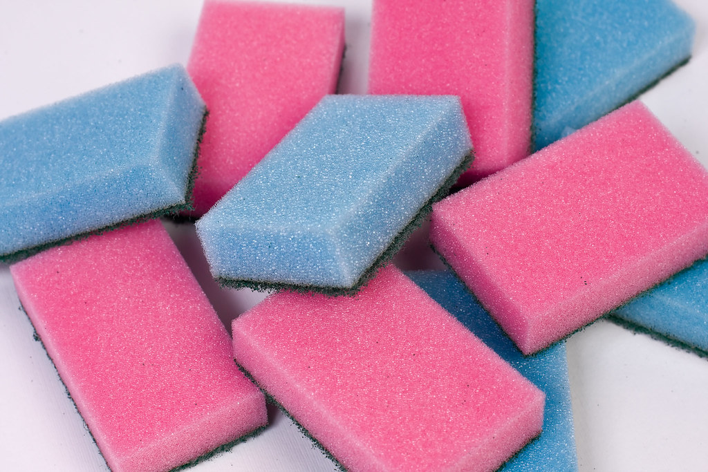 Blue and pink kitchen sponges stacked on a white surface
