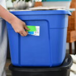 Hand placing a label on a blue plastic storage container