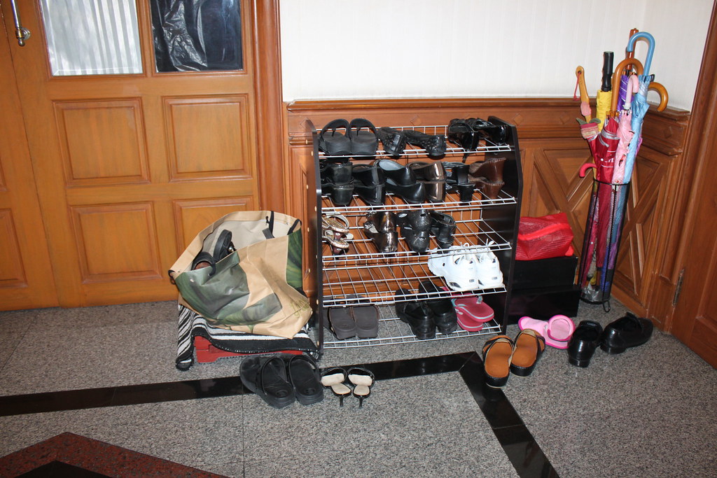Shoe rack with many shoes beside umbrellas near a wooden entry door