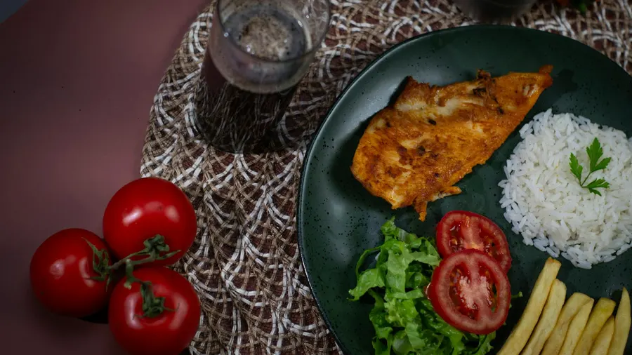Um prato vibrante com frango grelhado, arroz, salada e tomates, perfeito para uma refeição saudável.