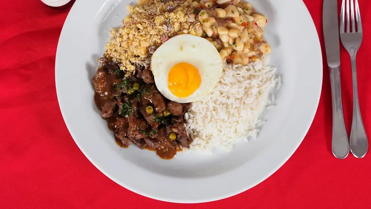 Uma vibrante refeição de feijoada brasileira com arroz, feijão e ovo frito em um fundo vermelho.