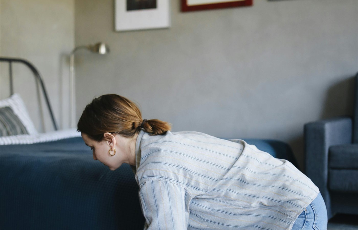 Person leaning down to clean a floor edge beside a low bed