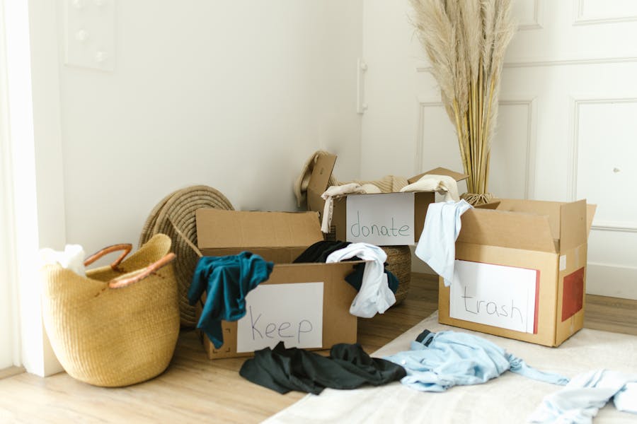 Boxes and loose clothing on the floor beside a white baseboard