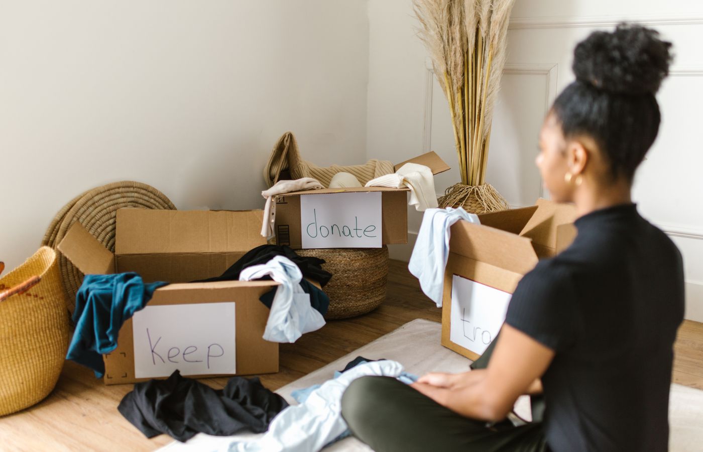 Person sorting clothes beside labeled decluttering boxes on the floor