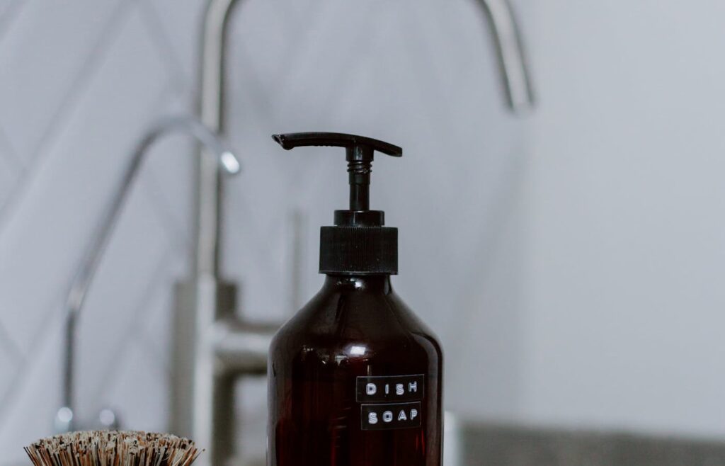 Dish soap bottle and scrub brush beside a kitchen sink