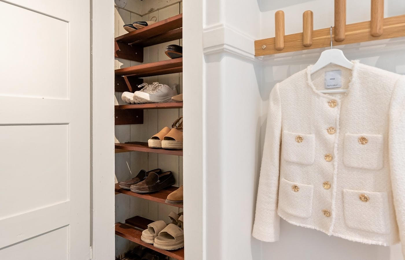 Small closet with shoe shelves and a white jacket on a hook