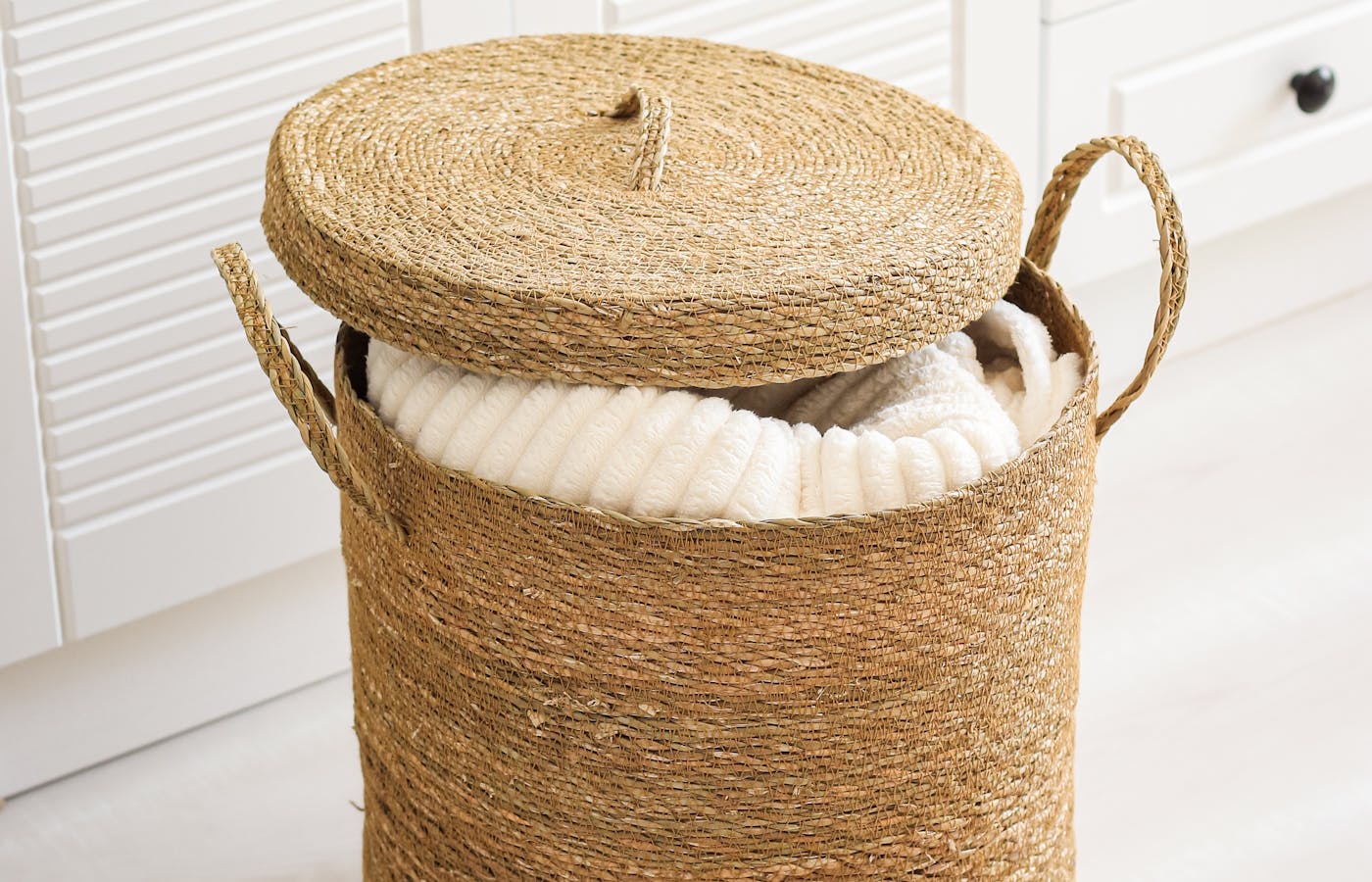 Woven lidded basket holding a white blanket in a bright room
