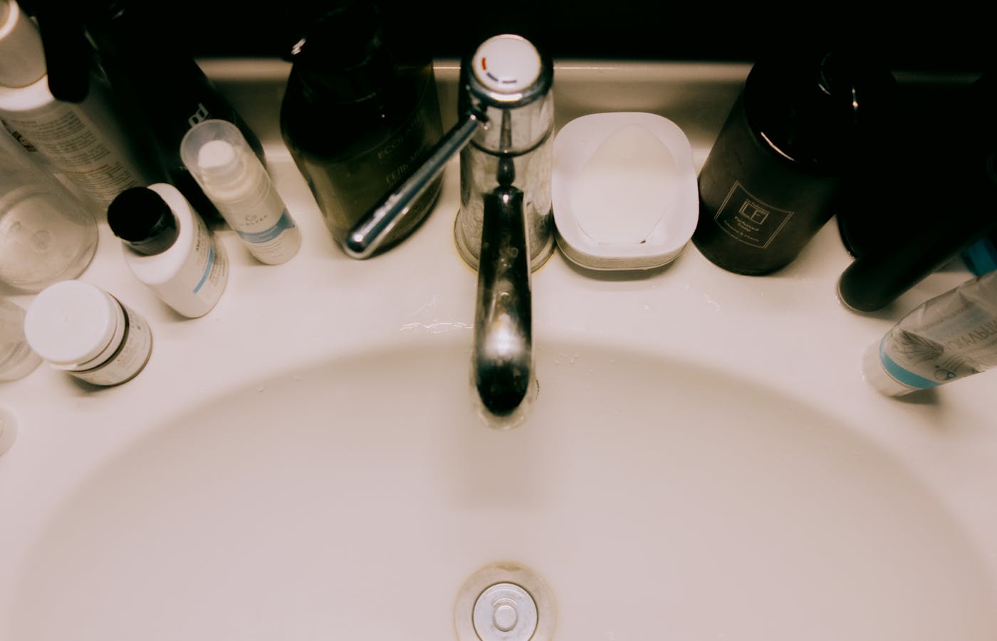 Bathroom sink with toiletries crowded around the faucet