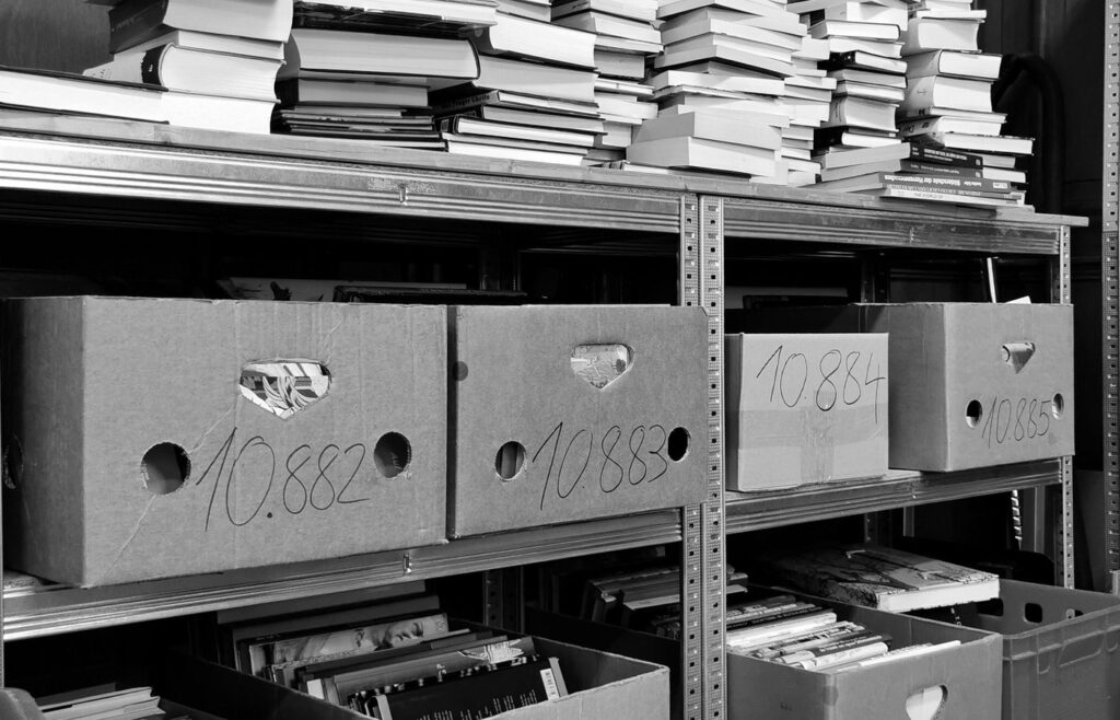 Cardboard storage boxes and stacks of books on metal shelves