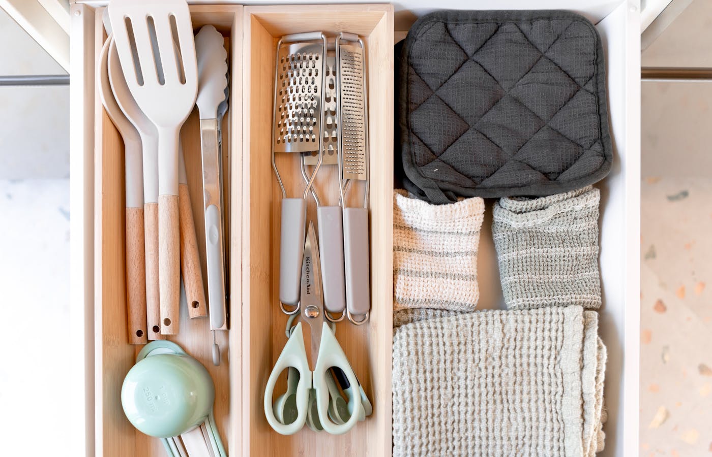 Organized kitchen drawer with utensils graters towels and wooden dividers