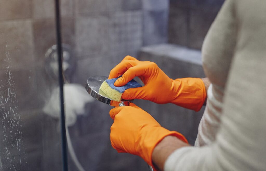Gloved hands cleaning a shower fixture with a sponge