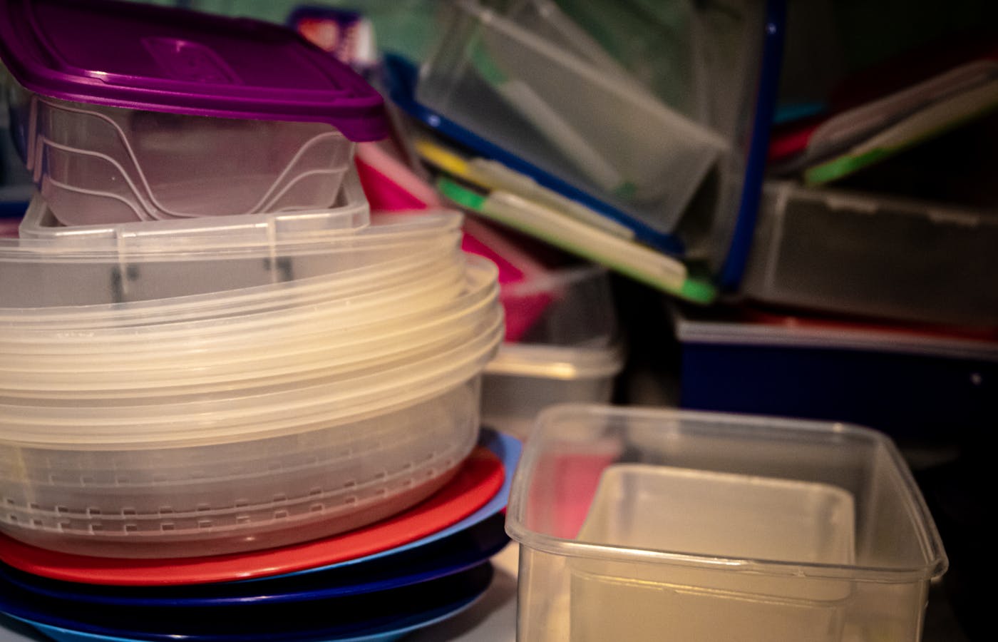 Plastic food containers and colorful lids stacked inside a cabinet