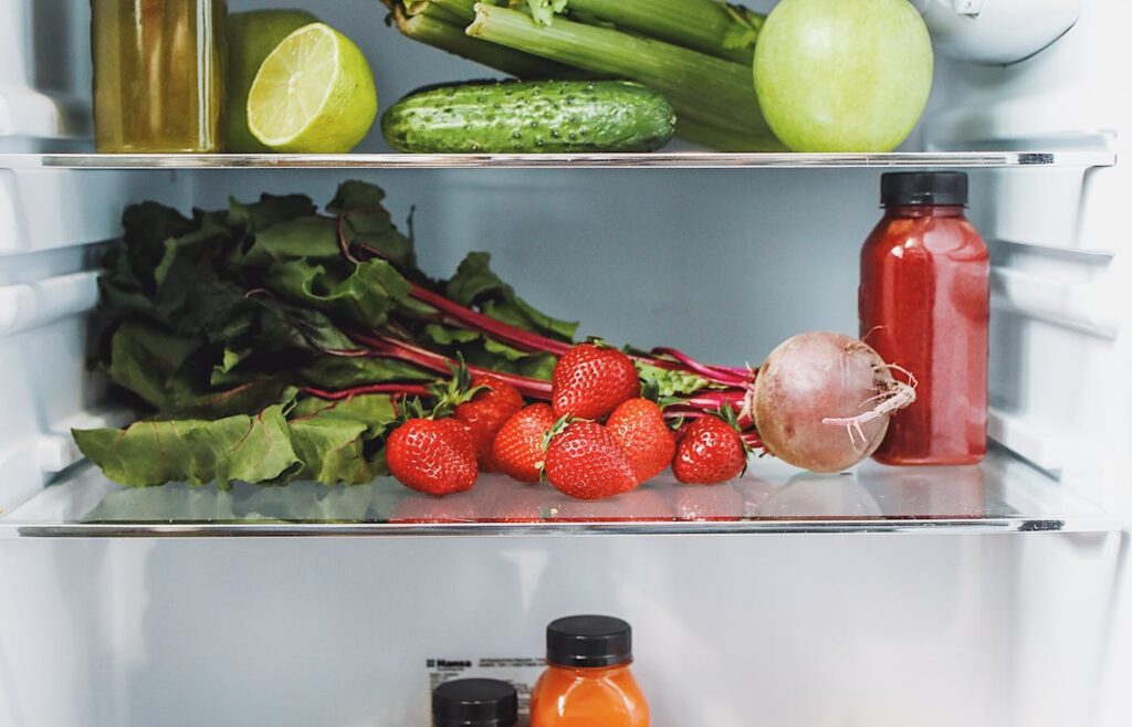 Fresh strawberries, beet greens, cucumber, celery, apple, and citrus inside a refrigerator