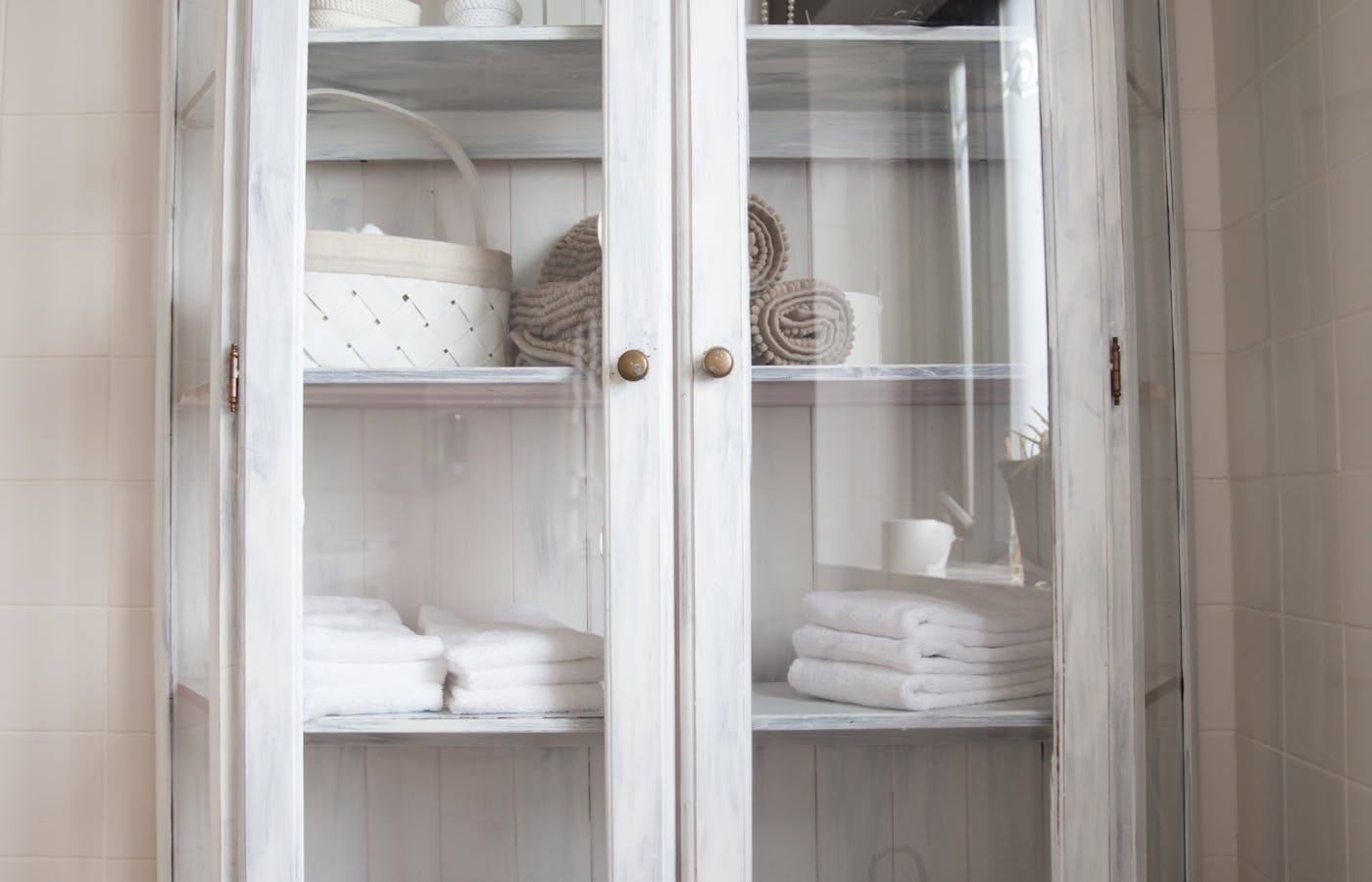White bathroom cabinet with folded towels and storage baskets behind glass doors