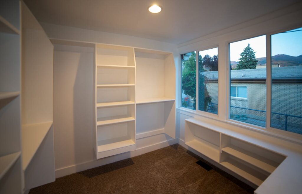 Empty white home organization shelves beside a large window