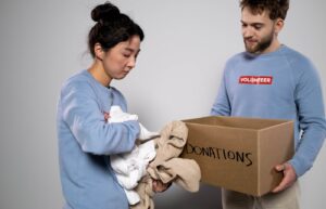 Person decluttering folded clothes into a cardboard donations box