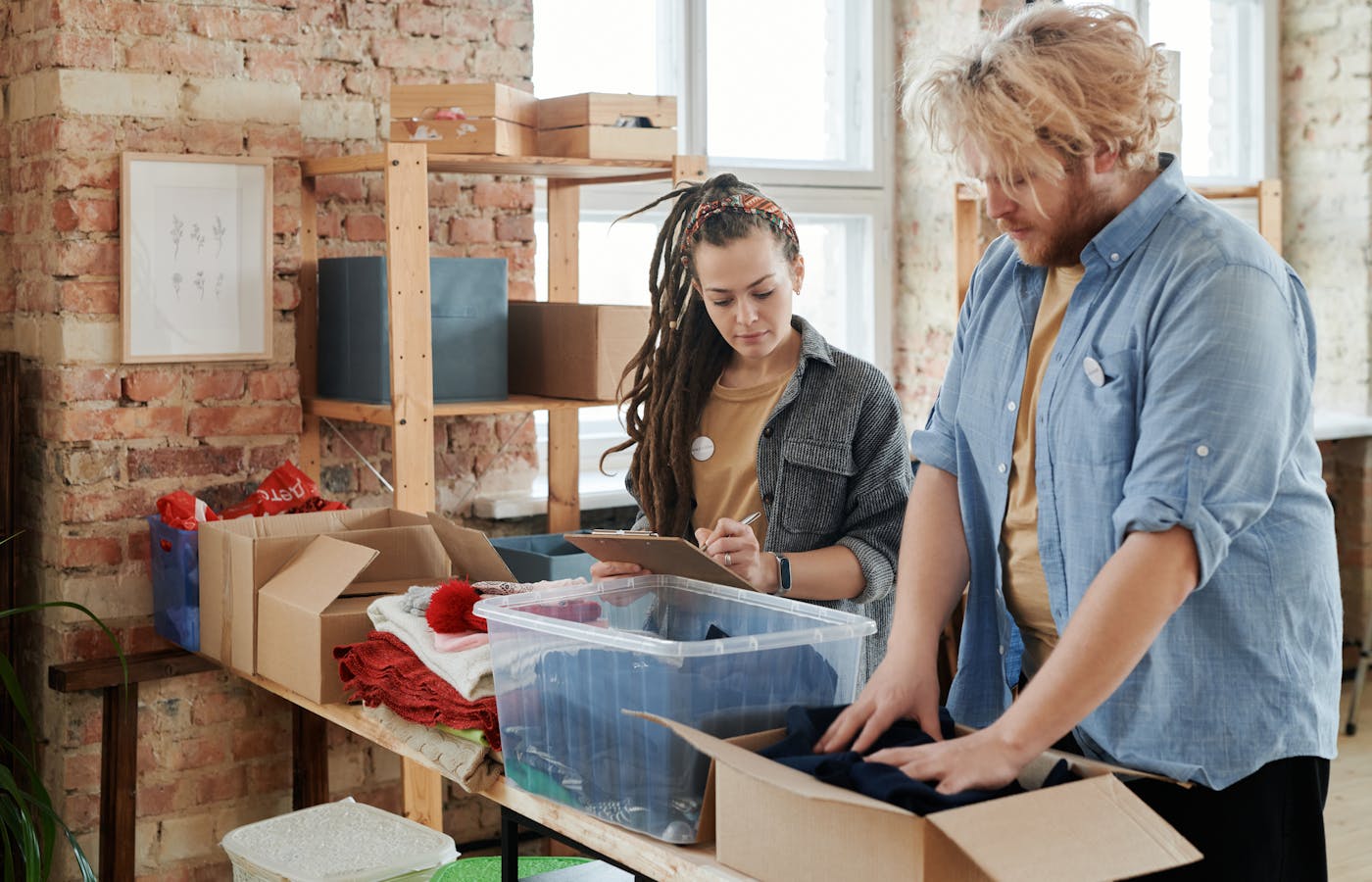 Two people decluttering clothes into a cardboard box and clear storage bin