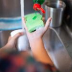 Person adding green dish soap to a sponge at a kitchen sink