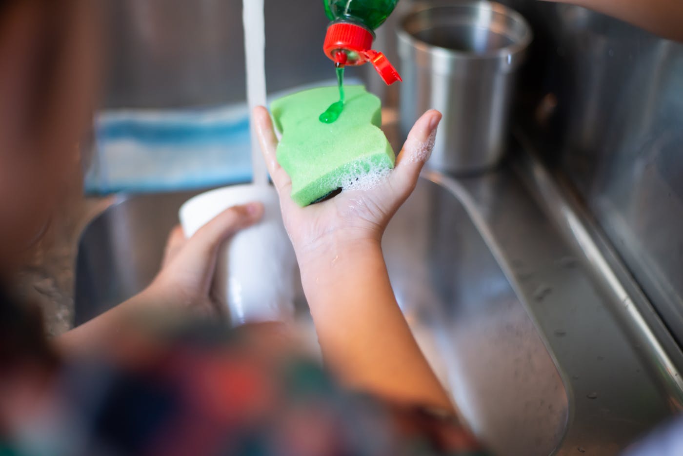 Person adding green dish soap to a sponge at a kitchen sink