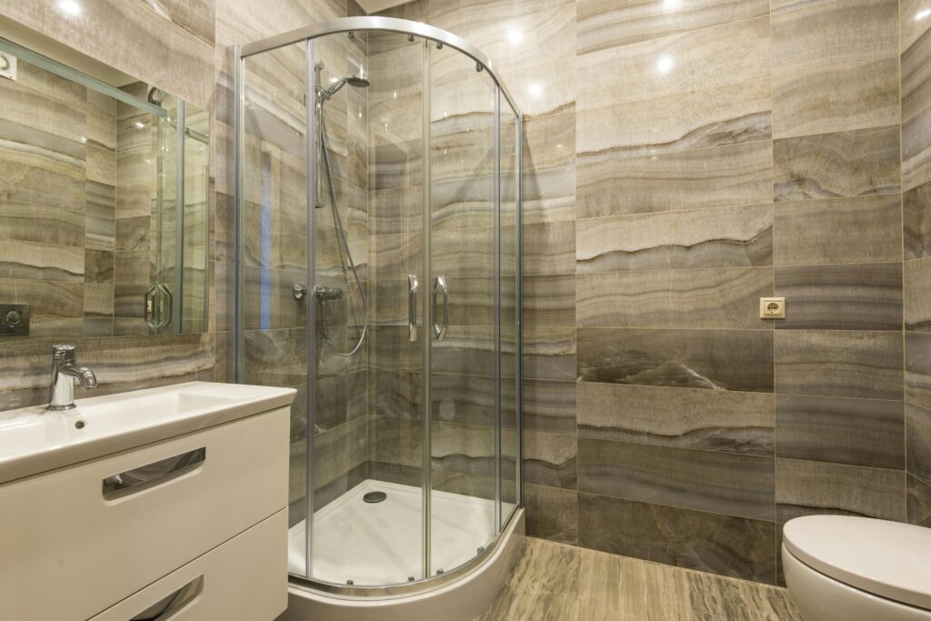Bathroom with curved glass shower doors and beige wall tiles