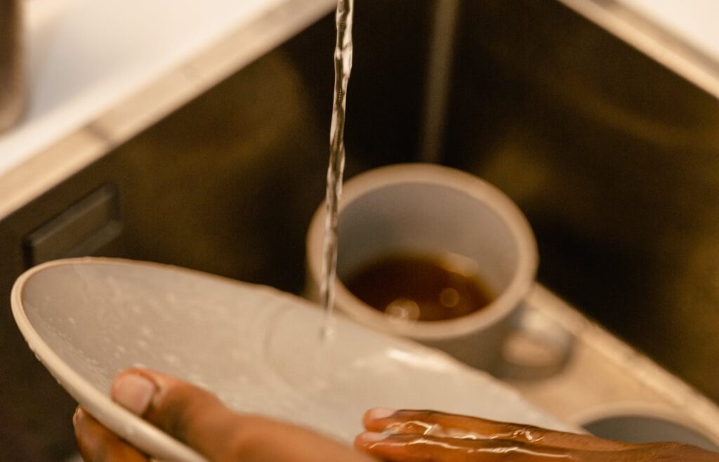 Hands rinsing a white bowl in a kitchen sink
