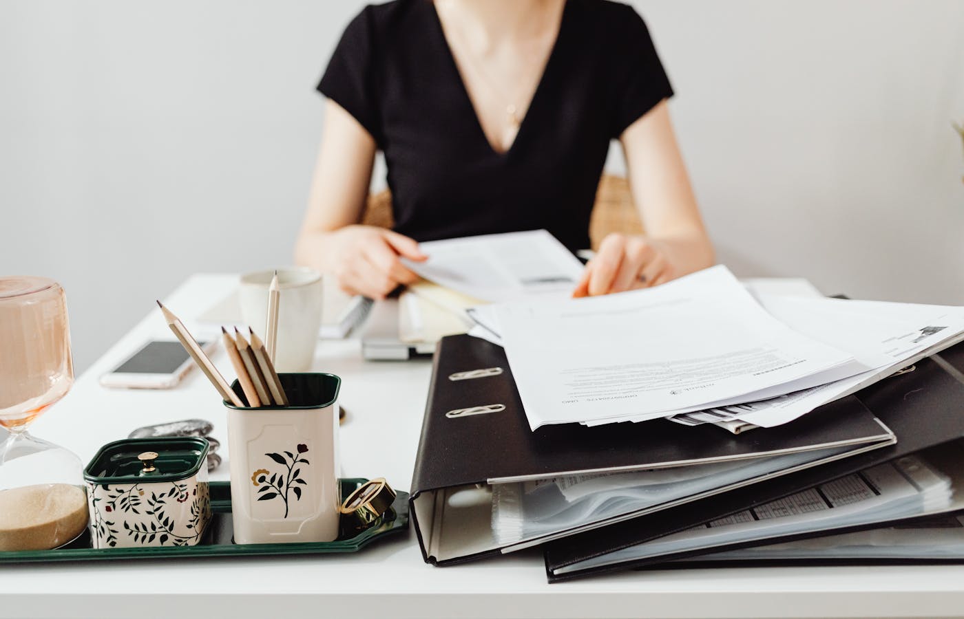 Person sorting paperwork beside a black binder on a desk