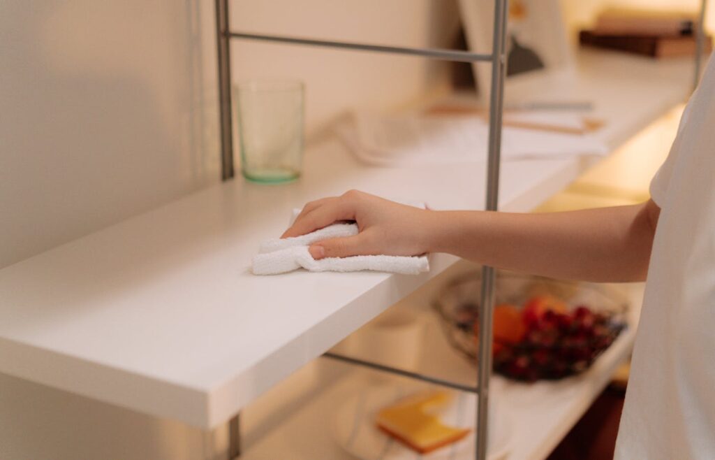 Hand dusting a white shelf with a folded cloth