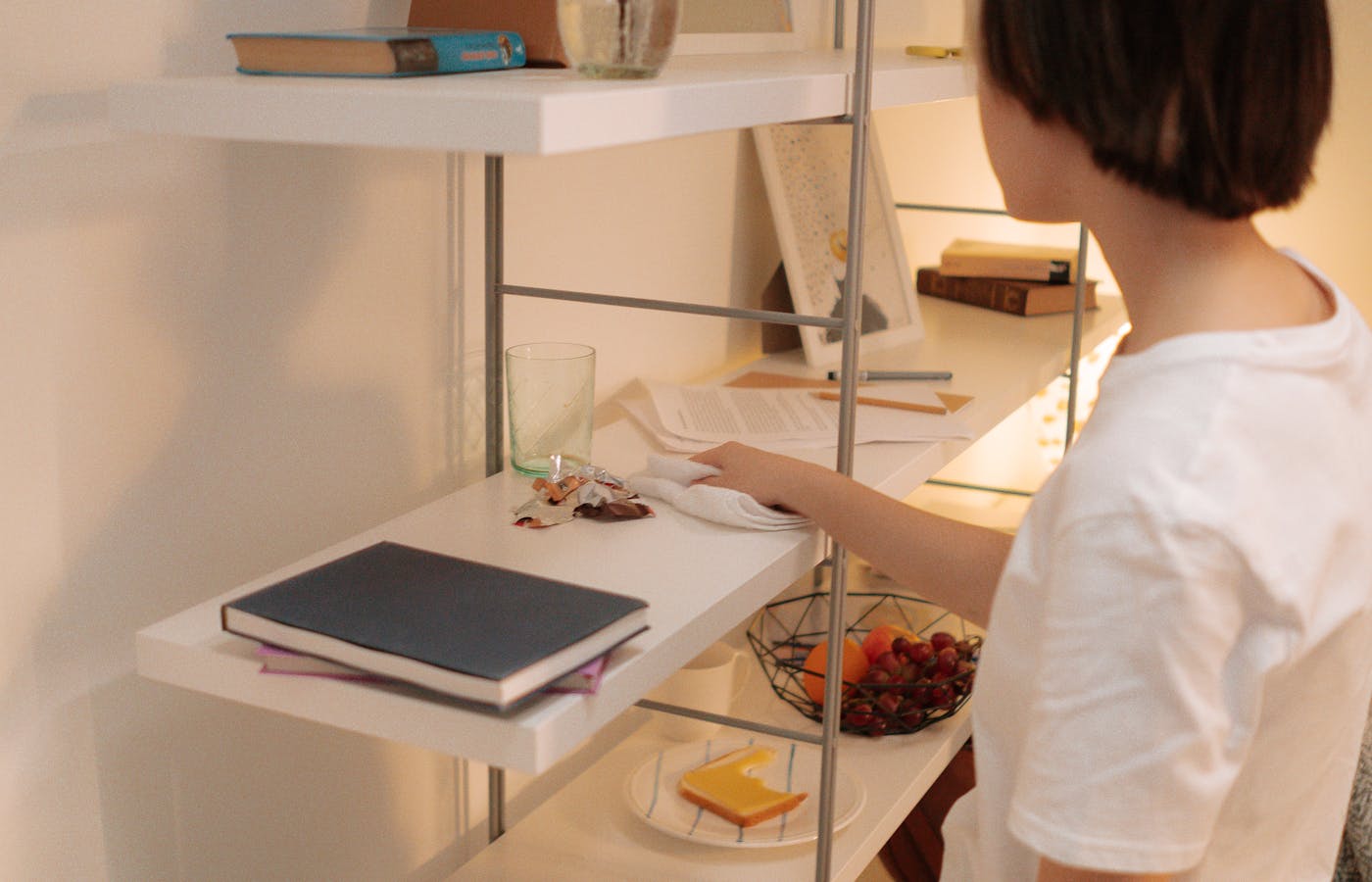 Person wiping dust from a white shelf with a cloth