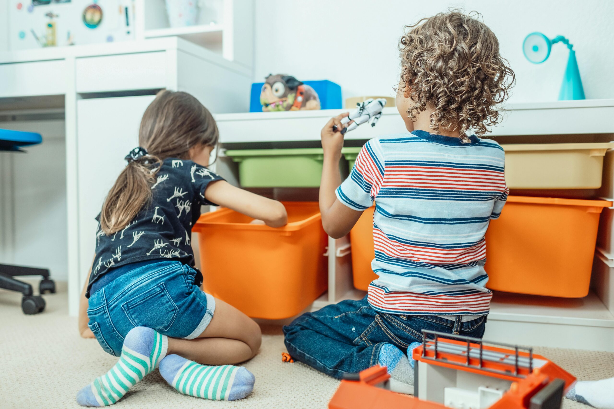 Children playing beside orange toy storage bins