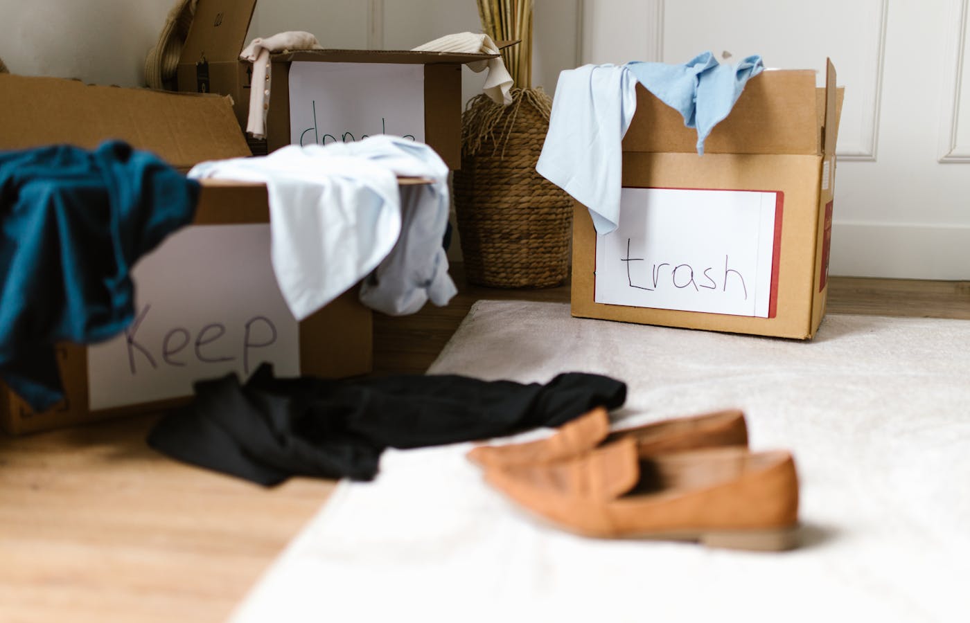 Decluttering boxes labeled keep, donate, and trash with clothes on the floor