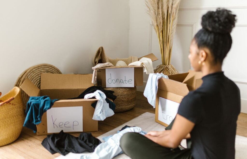 Person sorting clothes beside labeled decluttering boxes on the floor