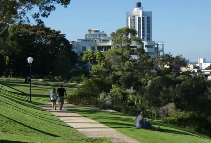 Parque ensolarado com pessoas caminhando e vista da cidade ao fundo