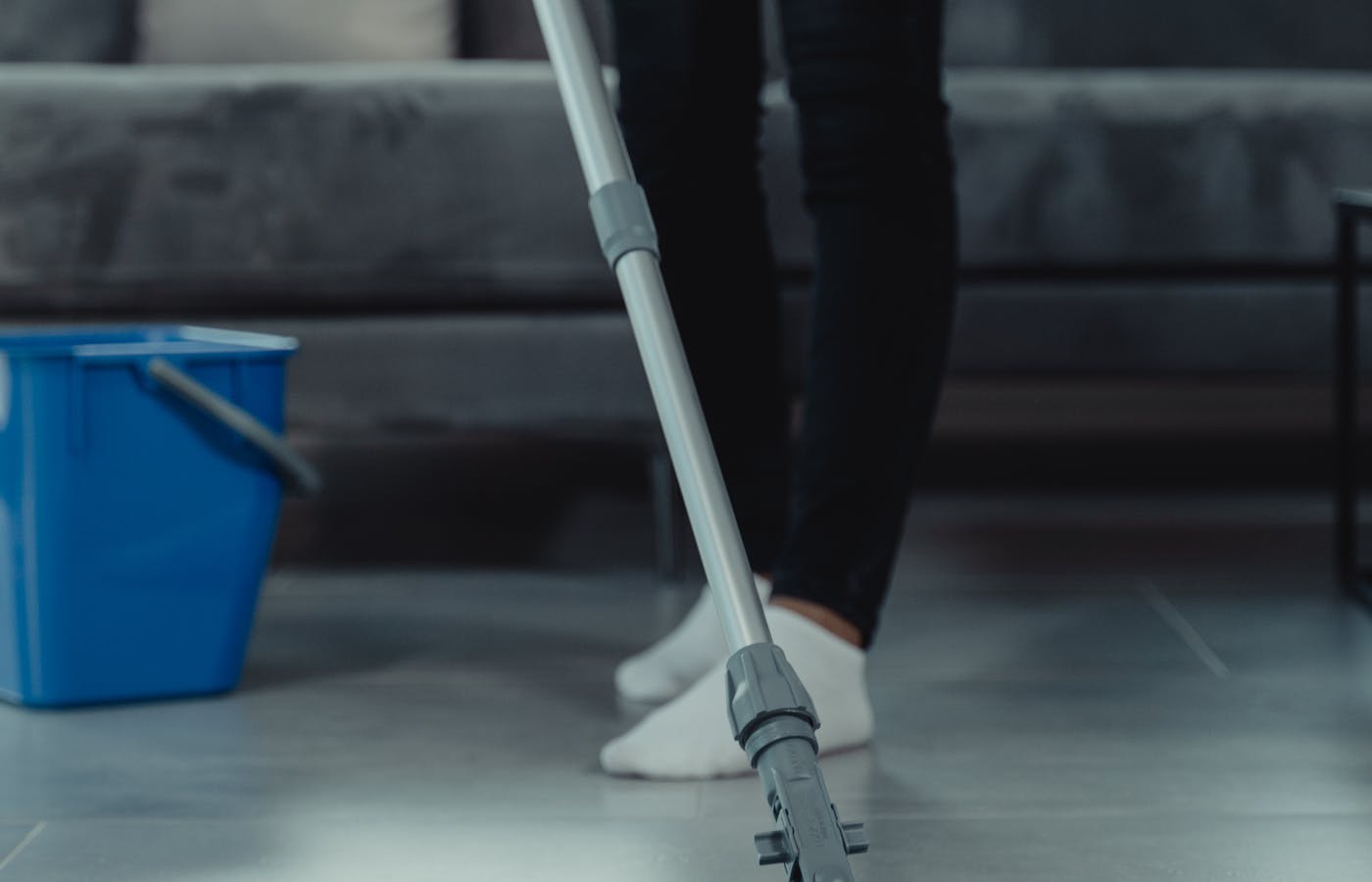 Mop handle on a floor beside a blue cleaning bucket