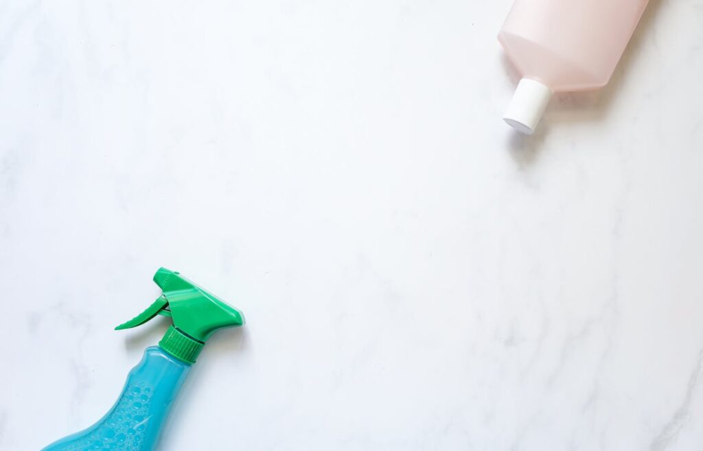 Blue spray bottle and pink cleaning bottle on a white surface